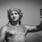Black and white photo of a Roman marble statue of a male figure holding an object, representing Venus theme