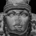 Ancient stone sculpture of a Roman goddess face with intricate headgear and side figures