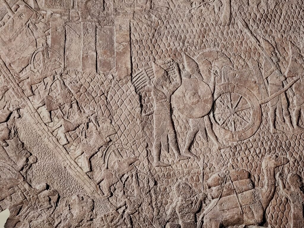 Ancient Assyrian stone relief of a battle scene with soldiers, chariots, and animals in motion
