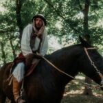 Man in traditional Middle Eastern attire riding a black horse through a forest, not a Tarbh Uisge folklore creature