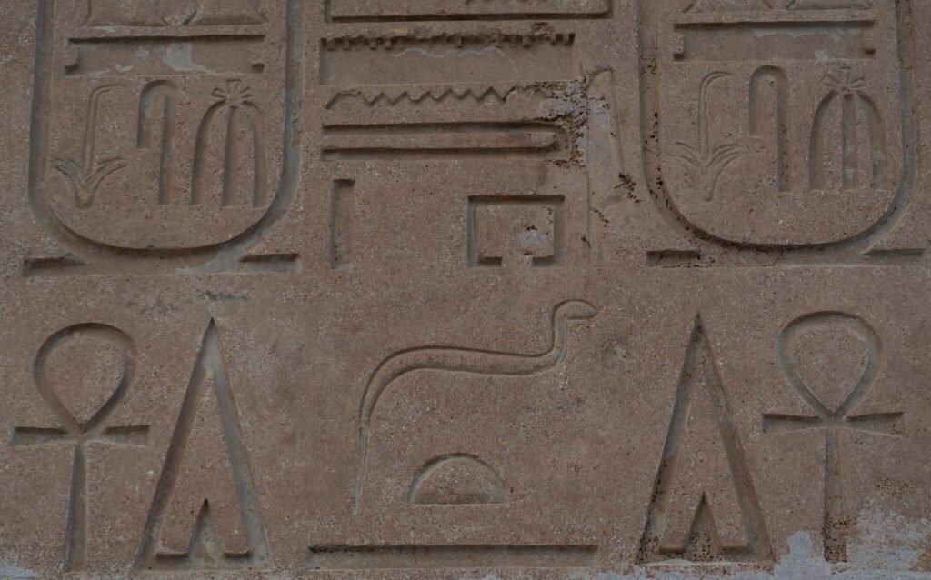 Ancient Egyptian hieroglyphs carved into a stone wall depicting a pharaoh with crook and flail symbols