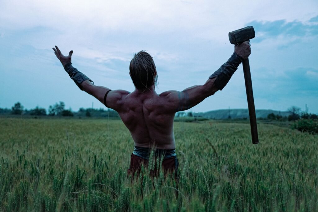Muscular Norse warrior holding an axe in a field beneath a cloudy sky, symbolizing strength and protection
