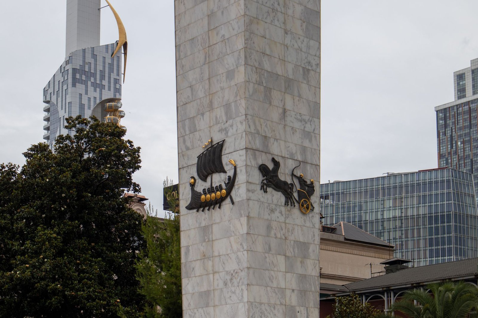 Tall stone monument with Viking ship and horse sculptures in a modern city, evoking Yggdrasil symbolism