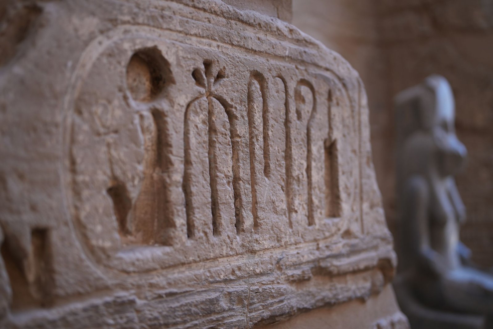 Close-up of ancient Egyptian hieroglyphs carved in stone with a blurred statue of an Egyptian deity in the background