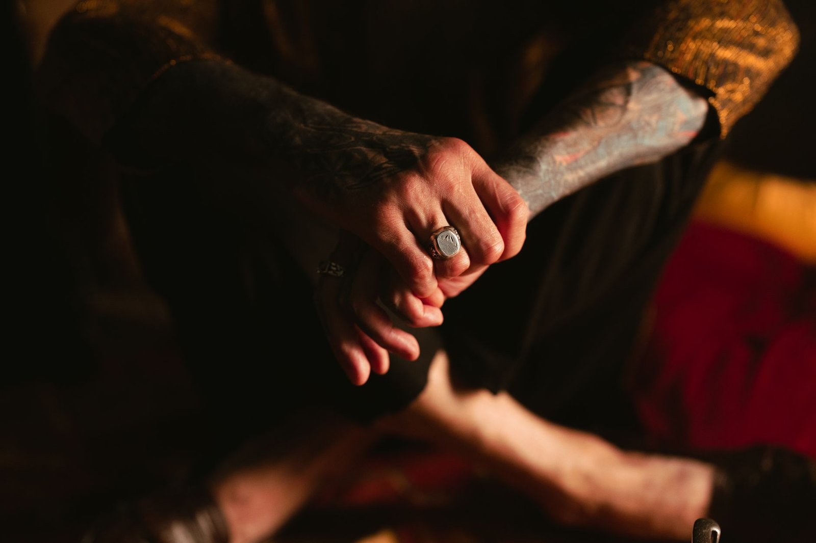 Tattooed person wearing rings sits barefoot in dim light, evoking Odin's ring Draupnir mythology