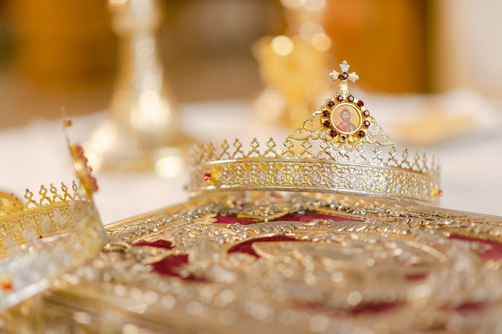 Ornate golden Egyptian crowns on a decorated surface, including an Atef crown with tall white plumes and central disk