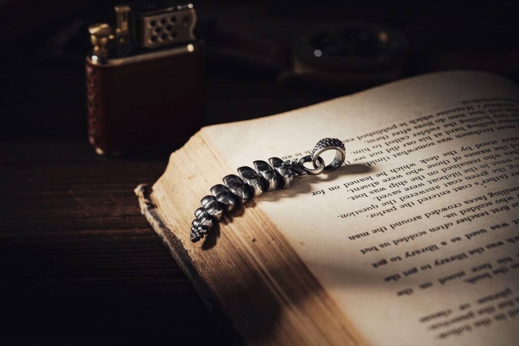 Vintage silver feather pendant on an open old book with a leather lighter behind it