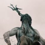 Bronze statue of Neptune holding the trident of Poseidon against a cloudy sky