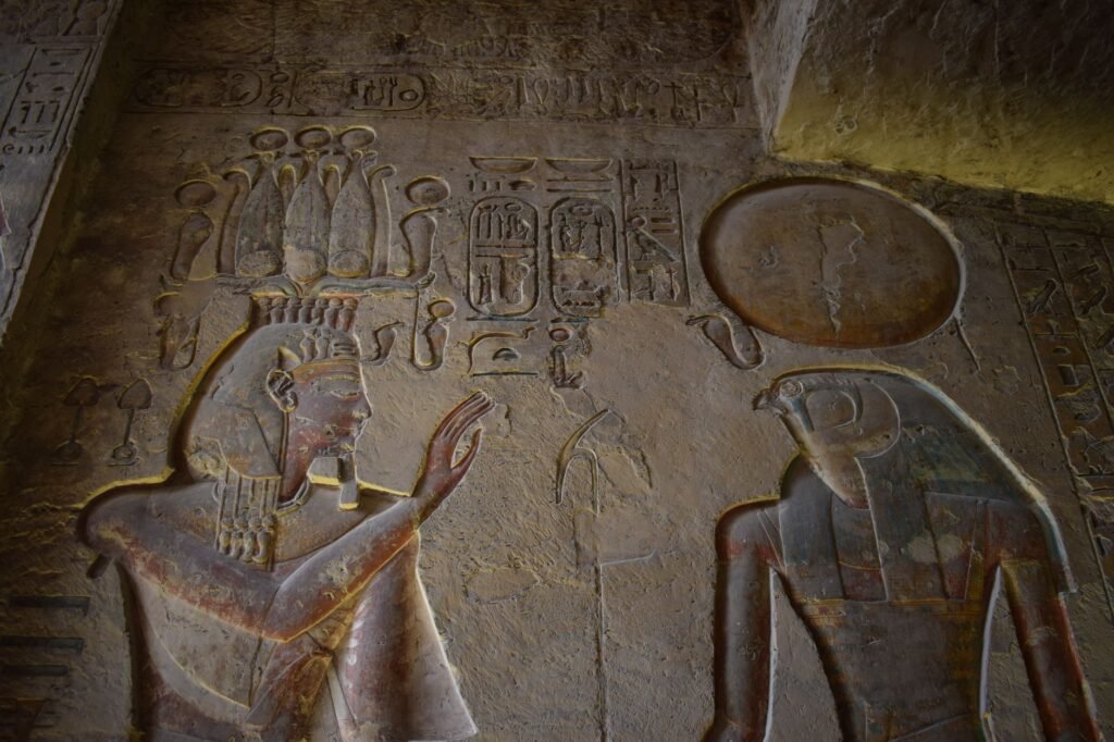 Ancient Egyptian temple wall carvings of deities, hieroglyphics, and a uraeus cobra on a sacred scene