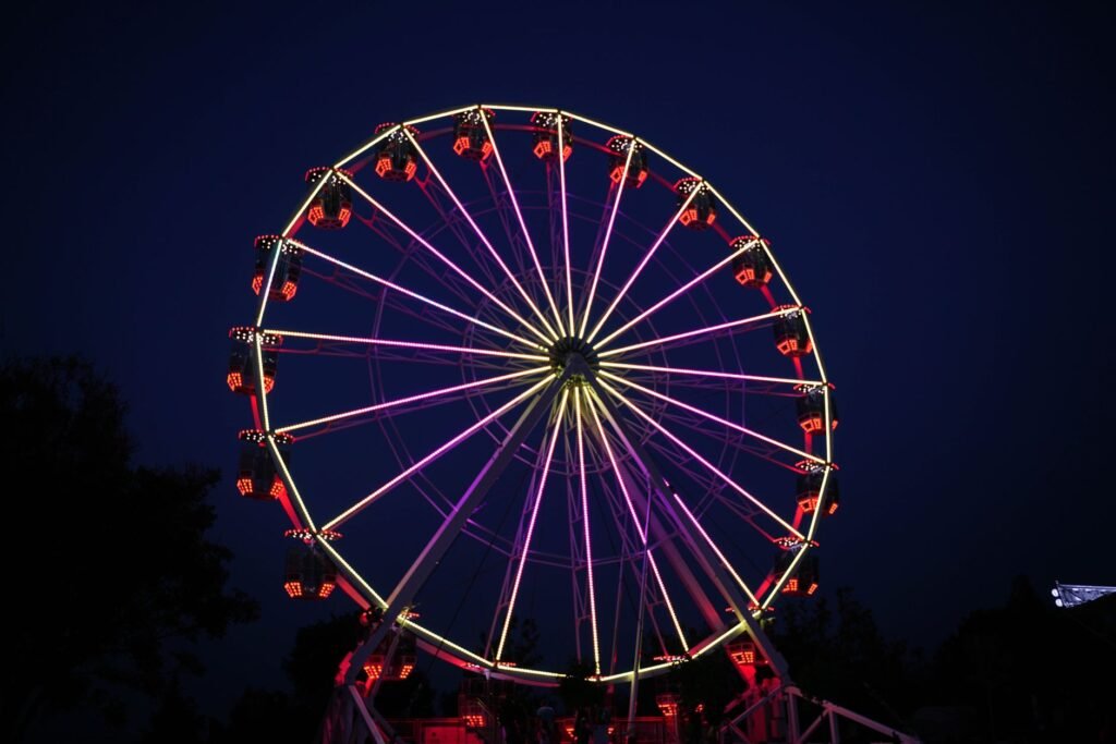 Illuminated Ferris wheel glowing with colorful lights against a dark night sky, resembling the Wheel of Taranis