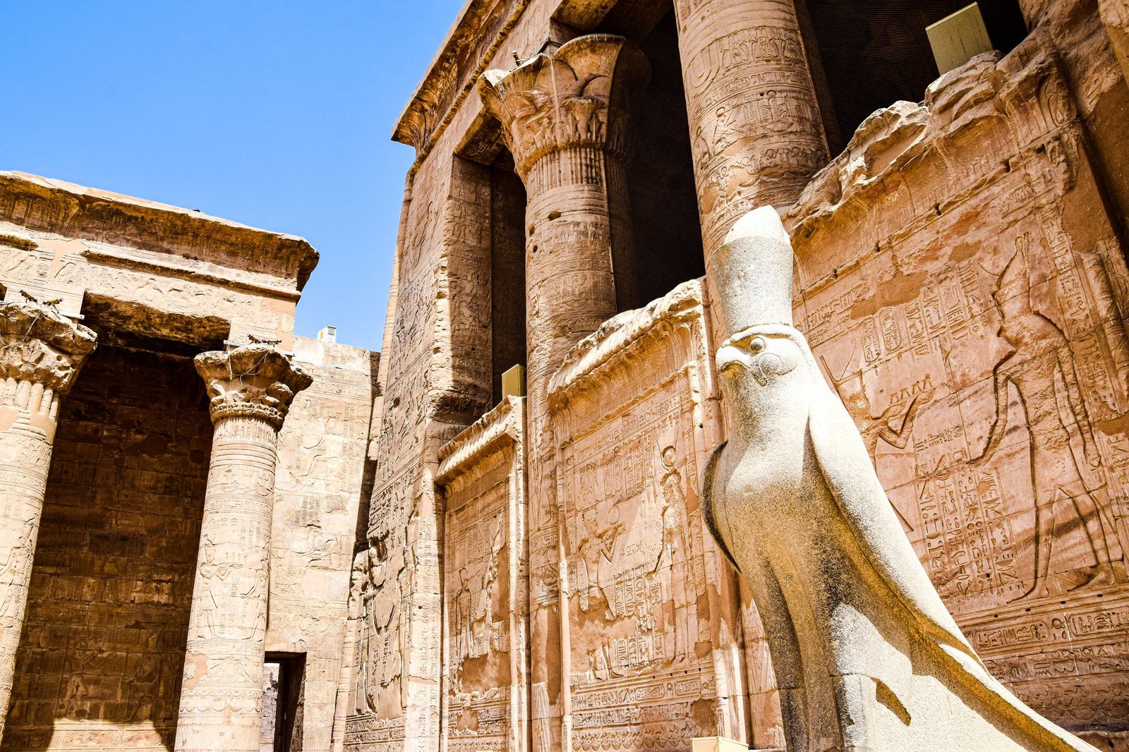 Ancient Egyptian temple ruins with carved statues and stone reliefs honoring the four sons of Horus under a blue sky