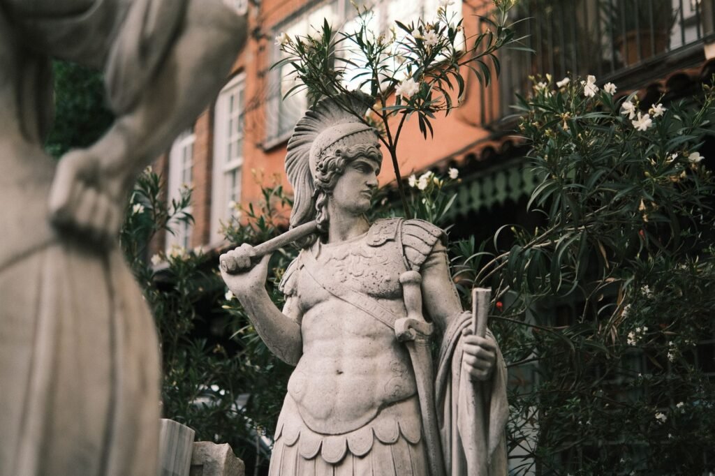 Ancient warrior statue with spear and shield representing Ares in Greek mythology in a garden setting