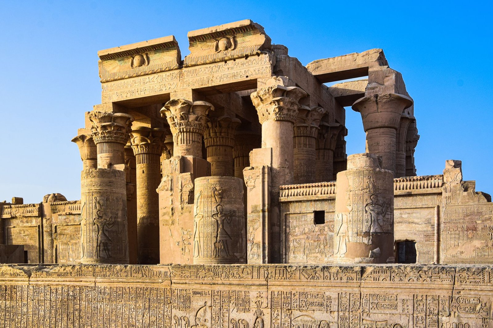Ancient Egyptian temple ruins with carved hieroglyphics beneath a clear blue sky, evoking Sobek, Nile god in mythology