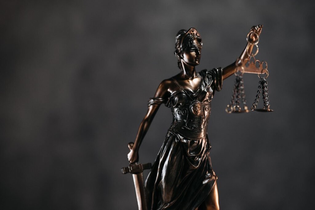 Bronze statue representing Themis in Greek mythology holding scales and a sword on a dark background