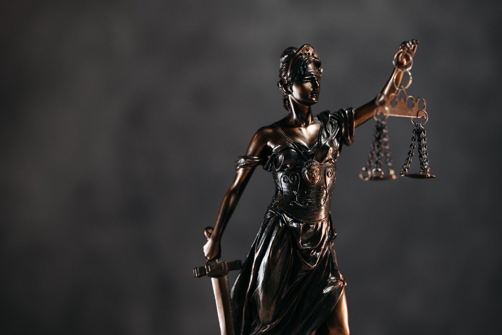 Bronze statue representing Themis in Greek mythology holding scales and a sword on a dark background