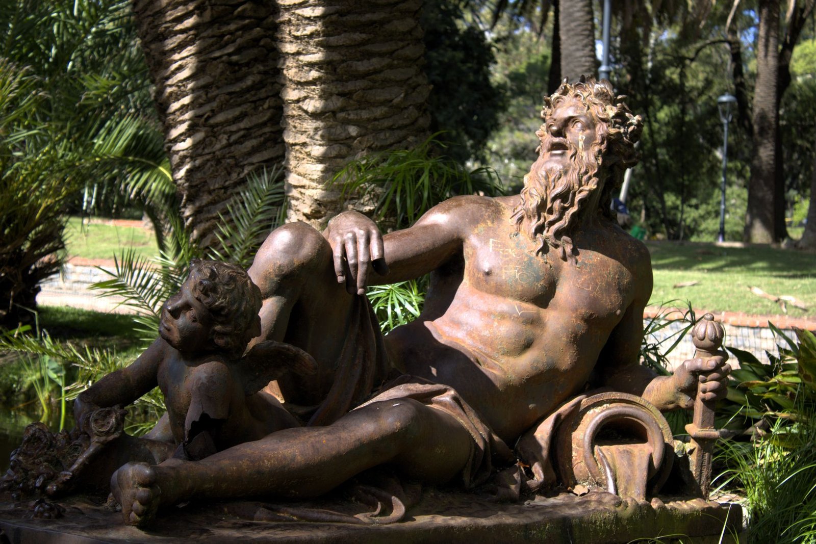 Bronze statue of reclining bearded Zeus in Greek mythology with two children in a lush garden