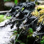 Row of ornate black dragon water spouts in a traditional Japanese garden, evoking Yamata no Orochi legend