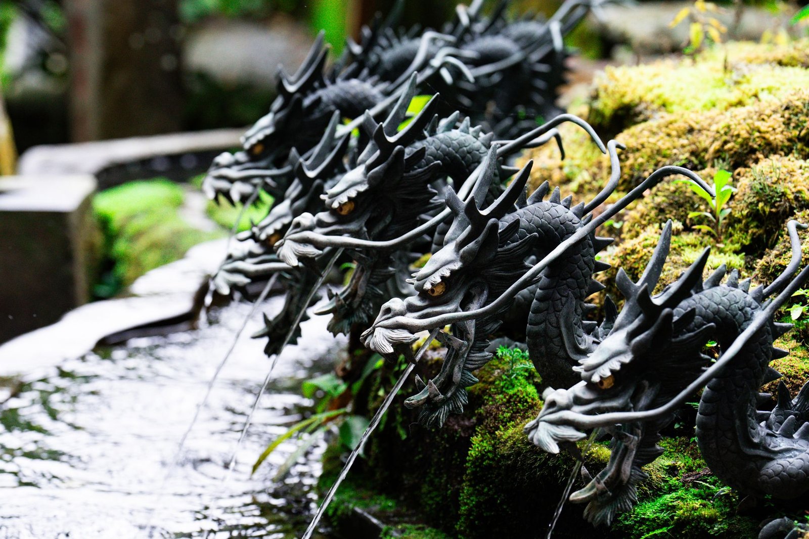 Row of ornate black dragon water spouts in a traditional Japanese garden, evoking Yamata no Orochi legend