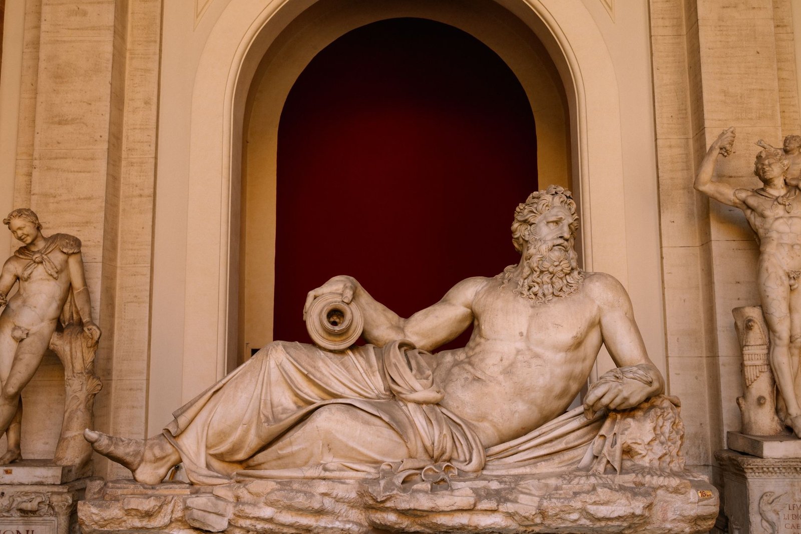 Ancient marble statues of reclining and standing male figures in a classical museum display