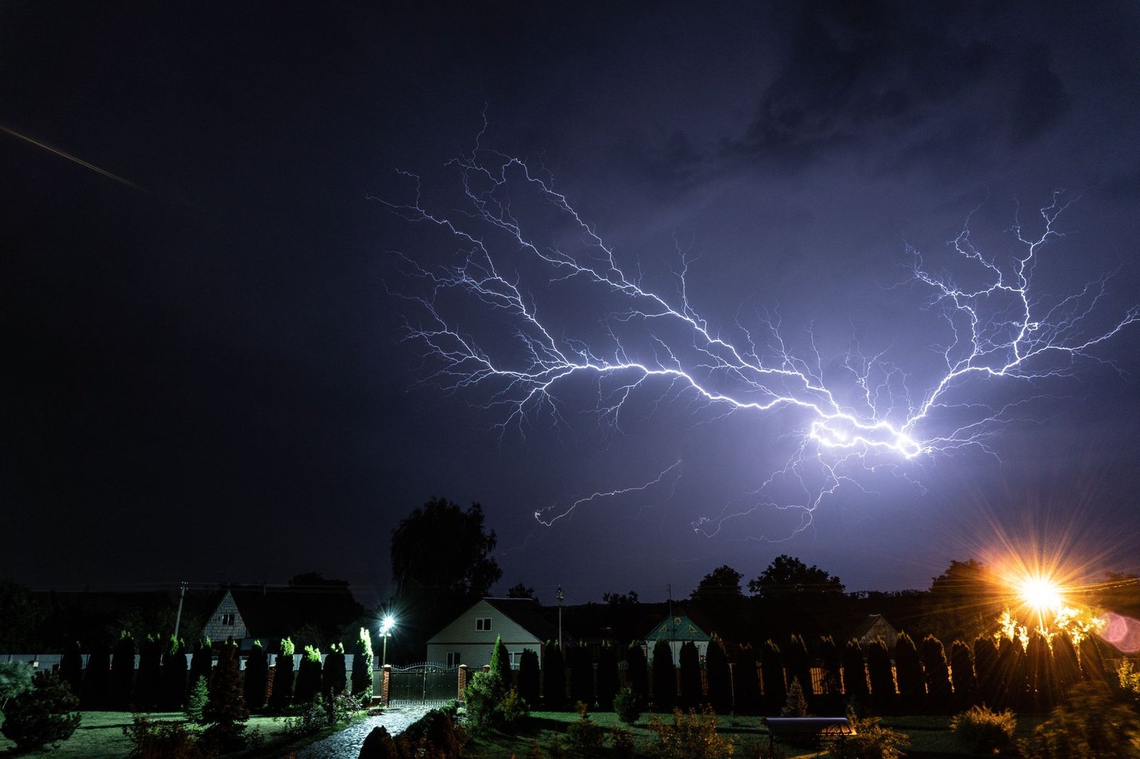 Lightning striking during a nighttime thunderstorm over a residential area, evoking Zeus’s thunderbolt